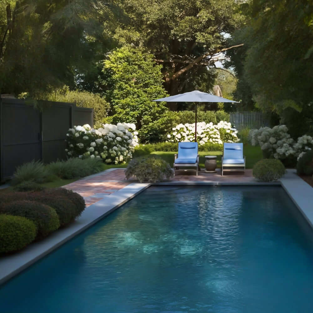 Notre entreprise conçoit des espaces extérieurs autour de piscines, en intégrant des éléments tels qu'un patio en pierre où sont disposés deux chaises longues et un parasol. La zone est entourée d'une végétation luxuriante et de fleurs blanches, ce qui confère au jardin une esthétique classique et apaisante. Nous visons à créer un environnement harmonieux qui invite à la détente, tout en respectant l'histoire et le caractère intemporel du lieu.